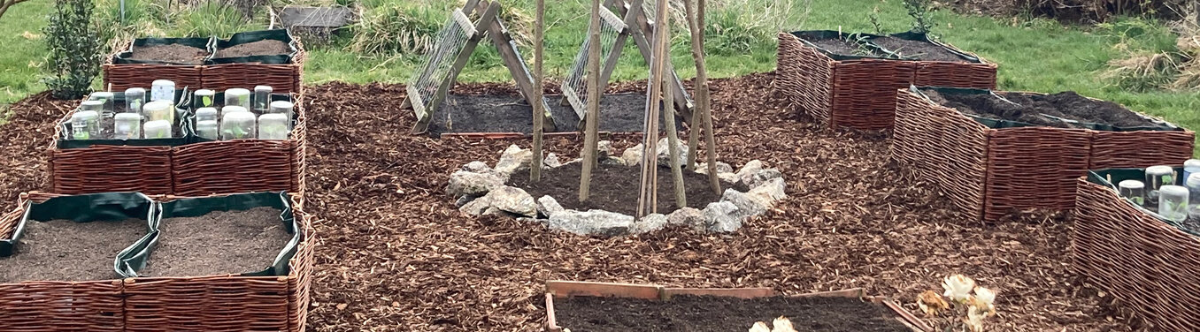 Garten im Frühling: geflochtene Hochbeete, Wege aus Holzhäcksel und ein Rankgerüst aus Stangen
